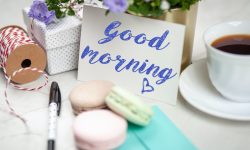 taza de té llena con platillo junto a la tarjeta de buenos días y bolígrafo y macarrones