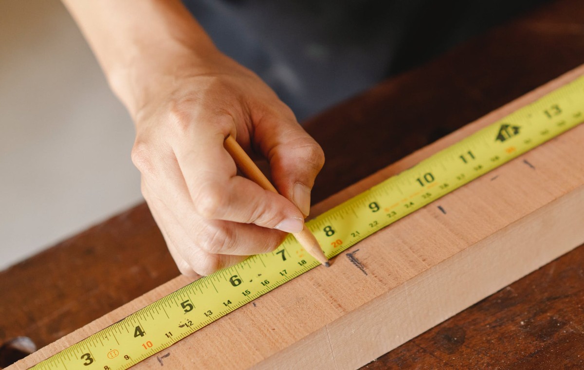 測定テープで木の板に印を付ける男性