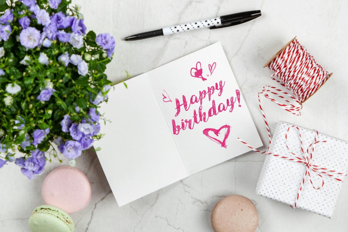 cartão de aniversário ao lado de uma caixa de flores e macarons